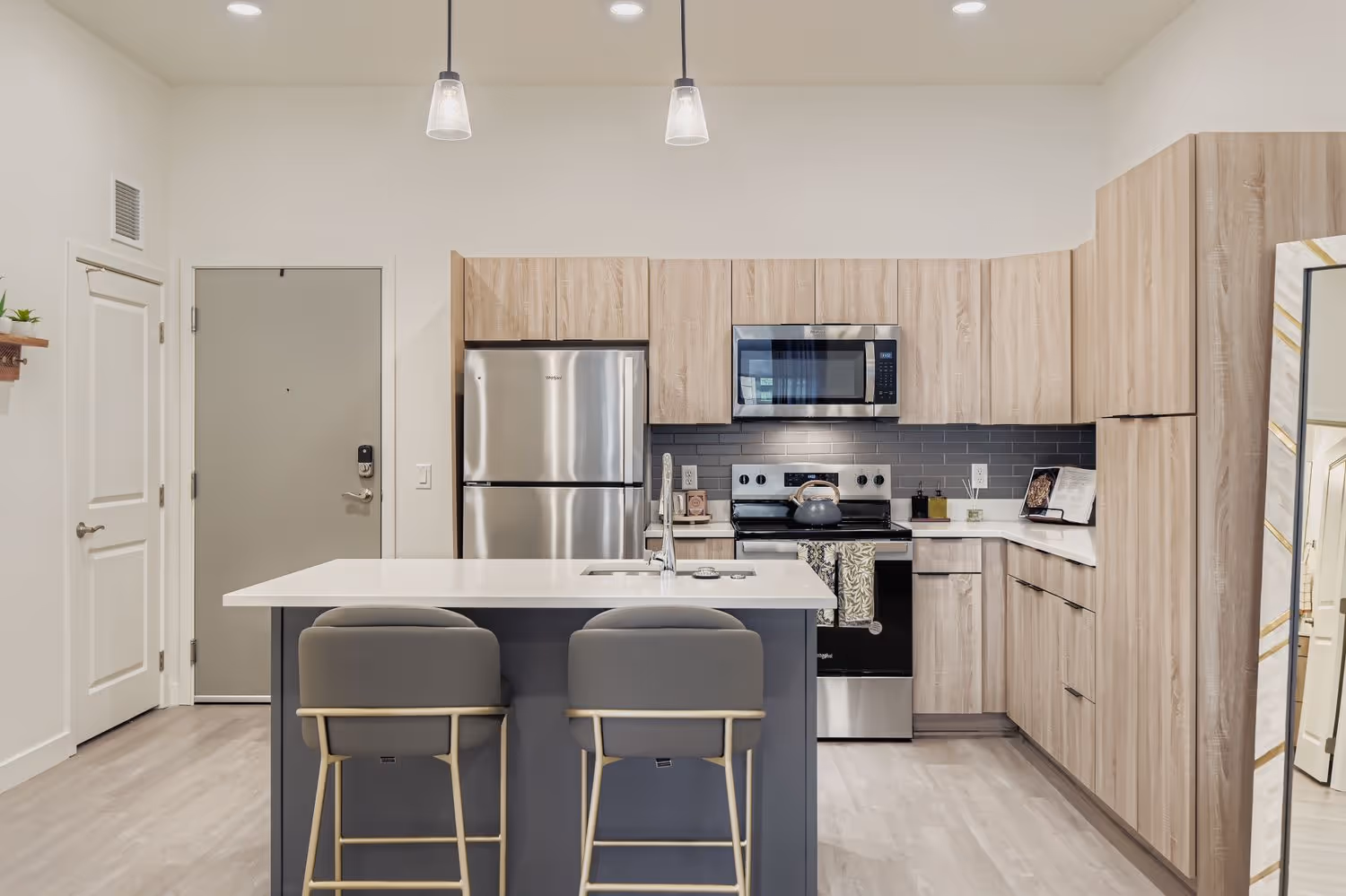 Open-concept apartment kitchen with light wood cabinetry, stainless steel appliances, and a kitchen island, overlooking the living area at Crossing at 9th in Salt Lake City.