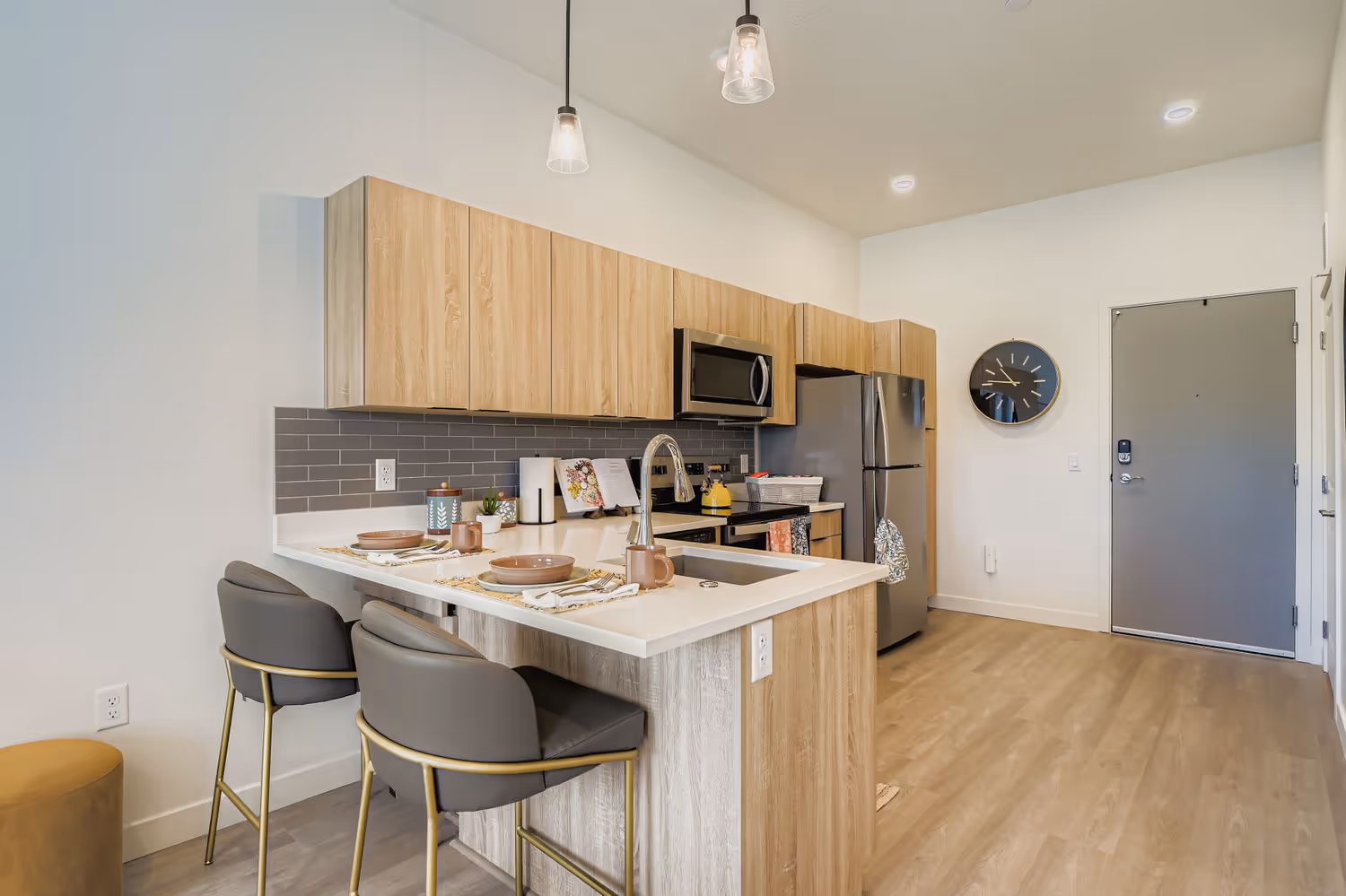 Contemporary kitchen with light wood-grain cabinets, stainless steel appliances, a kitchen island with bar stools, and pendant lighting, at Crossing at 9th in Salt Lake City.