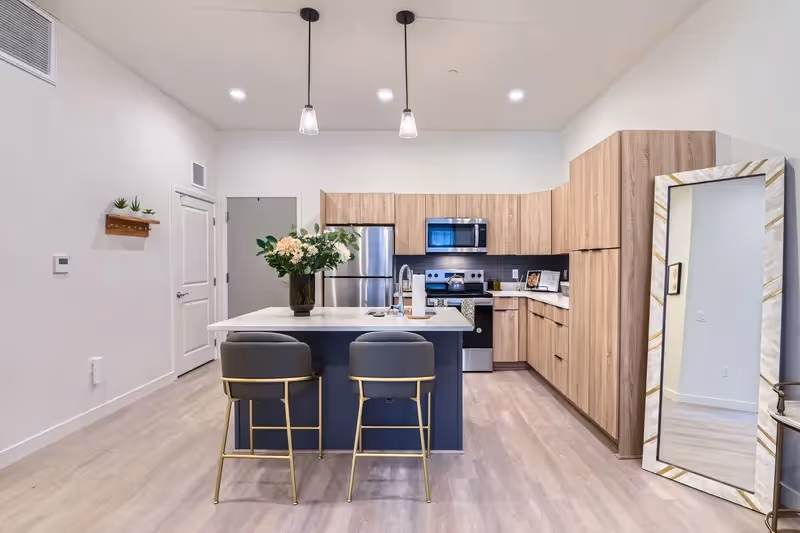 Modern kitchen with two-tone cabinetry, a large island with bar stools, and stainless steel appliances, characteristic of apartments at Crossing at 9th in Salt Lake City.