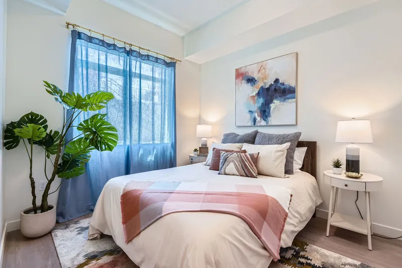 Bright bedroom with a large bed, blue curtains, and modern art, showcasing an apartment interior at Crossing at 9th in Salt Lake City.