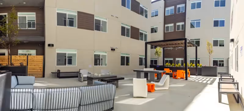 Spacious outdoor courtyard with various seating areas, including lounge sofas and dining tables, surrounded by apartment buildings at Crossing at 9th in Salt Lake City.