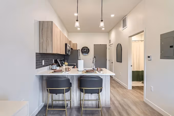 Open-concept apartment kitchen with light wood cabinetry, stainless steel appliances, and a kitchen island, overlooking the living area at Crossing at 9th in Salt Lake City.