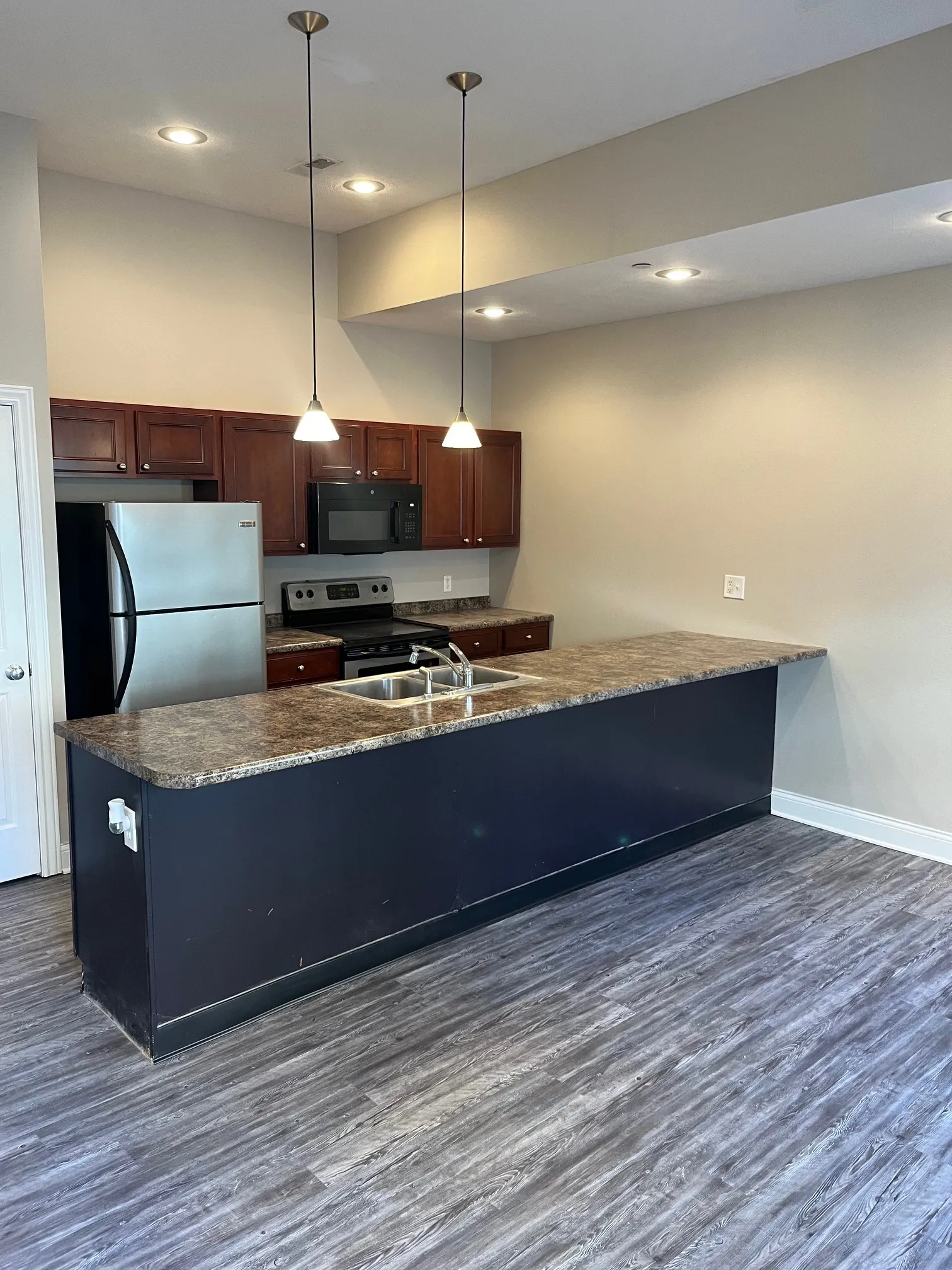 Modern kitchen at 5 North in Bloomington featuring a large breakfast bar island, stainless steel refrigerator, and dark wood cabinetry.
