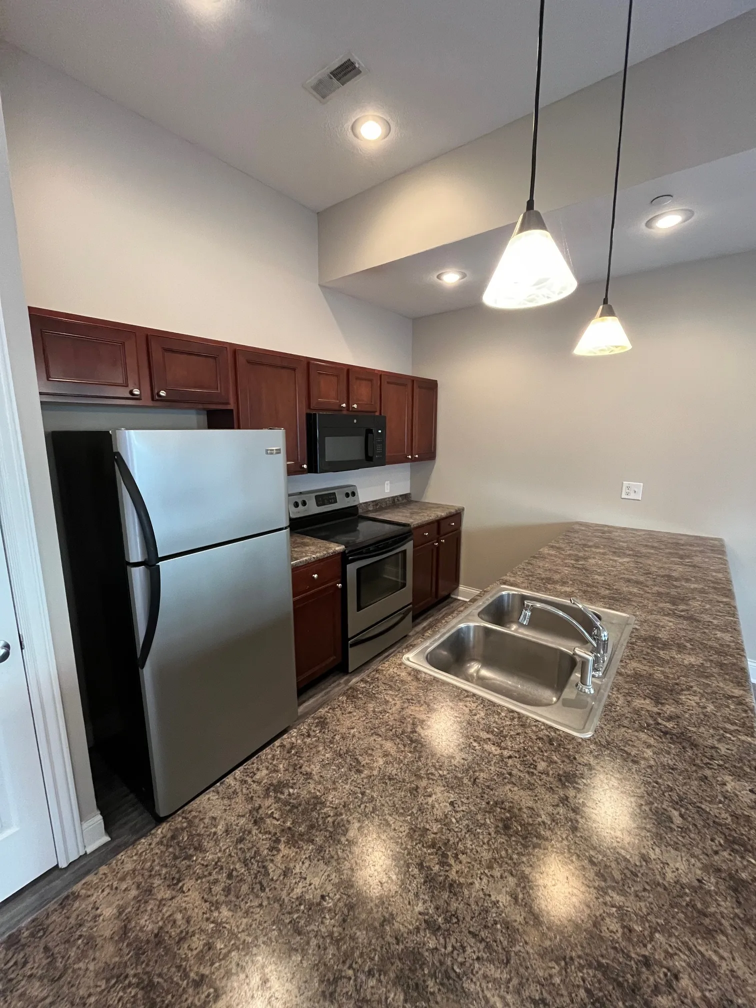 Modern kitchen at 5 North with stainless steel appliances, dark wood cabinetry, granite-look countertops, and pendant lighting.