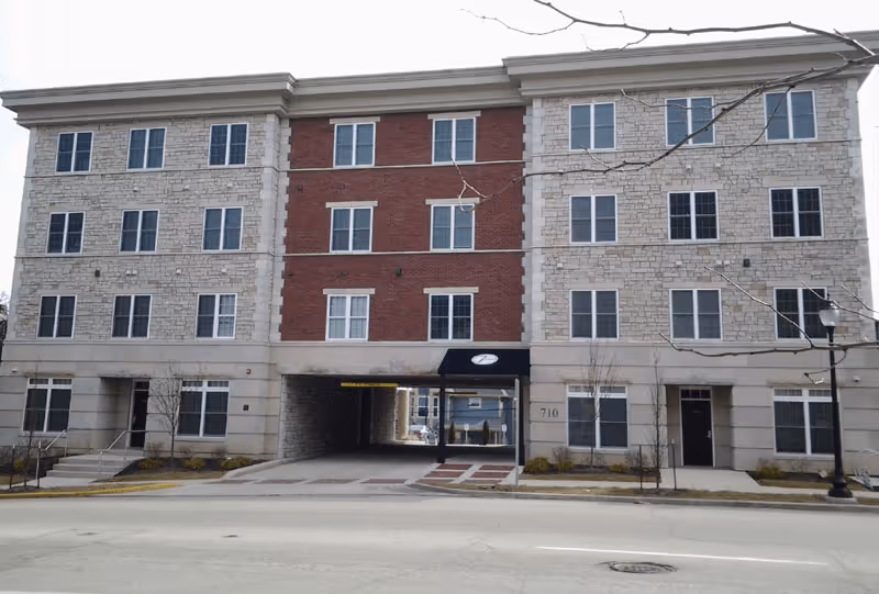 Multi-story 7 Ten residential building featuring tan siding, white trim, and a covered ground-level parking area.