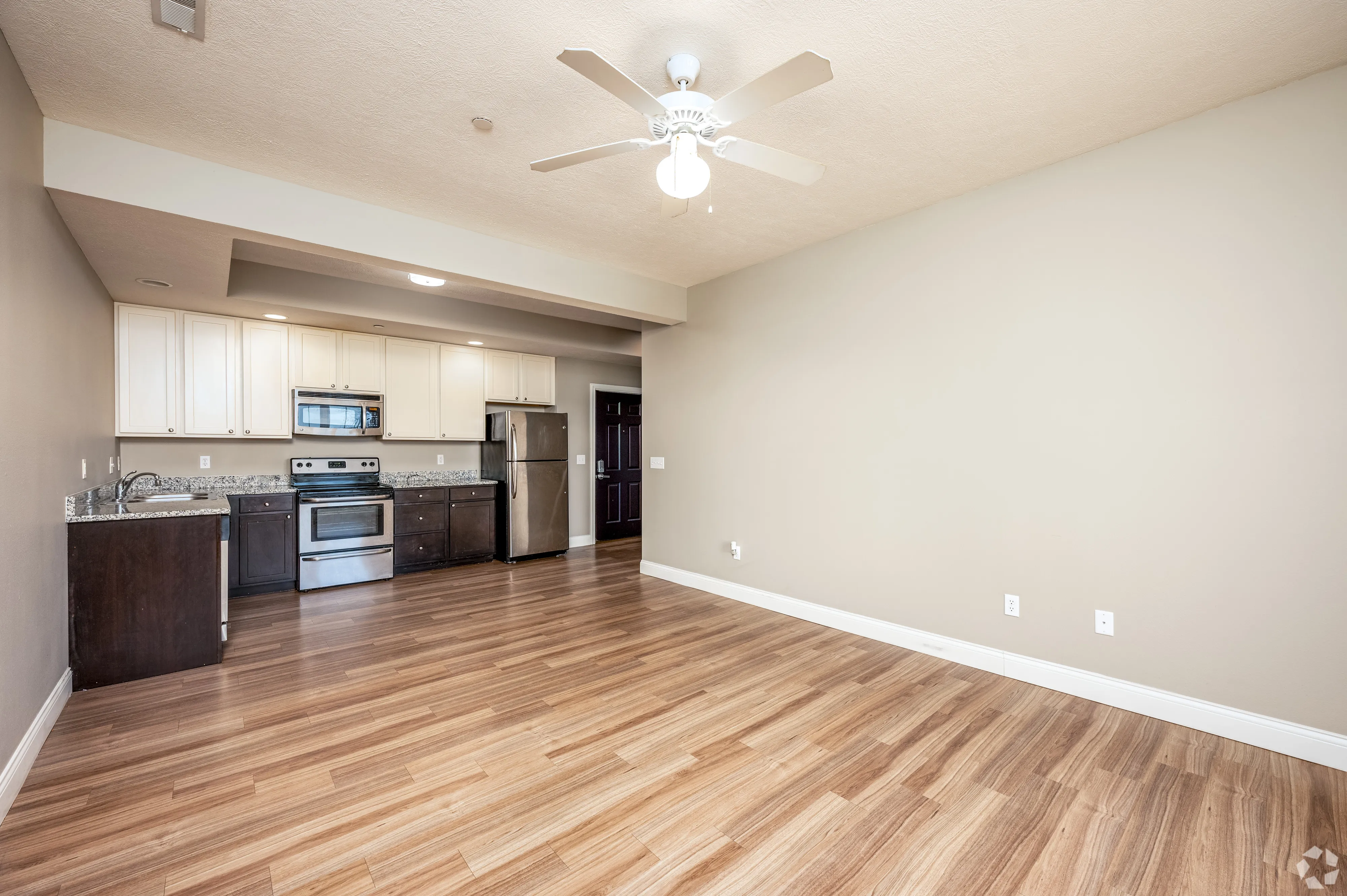 Open-concept living area at 7 Ten with wood-style flooring, neutral walls, and a white ceiling fan.