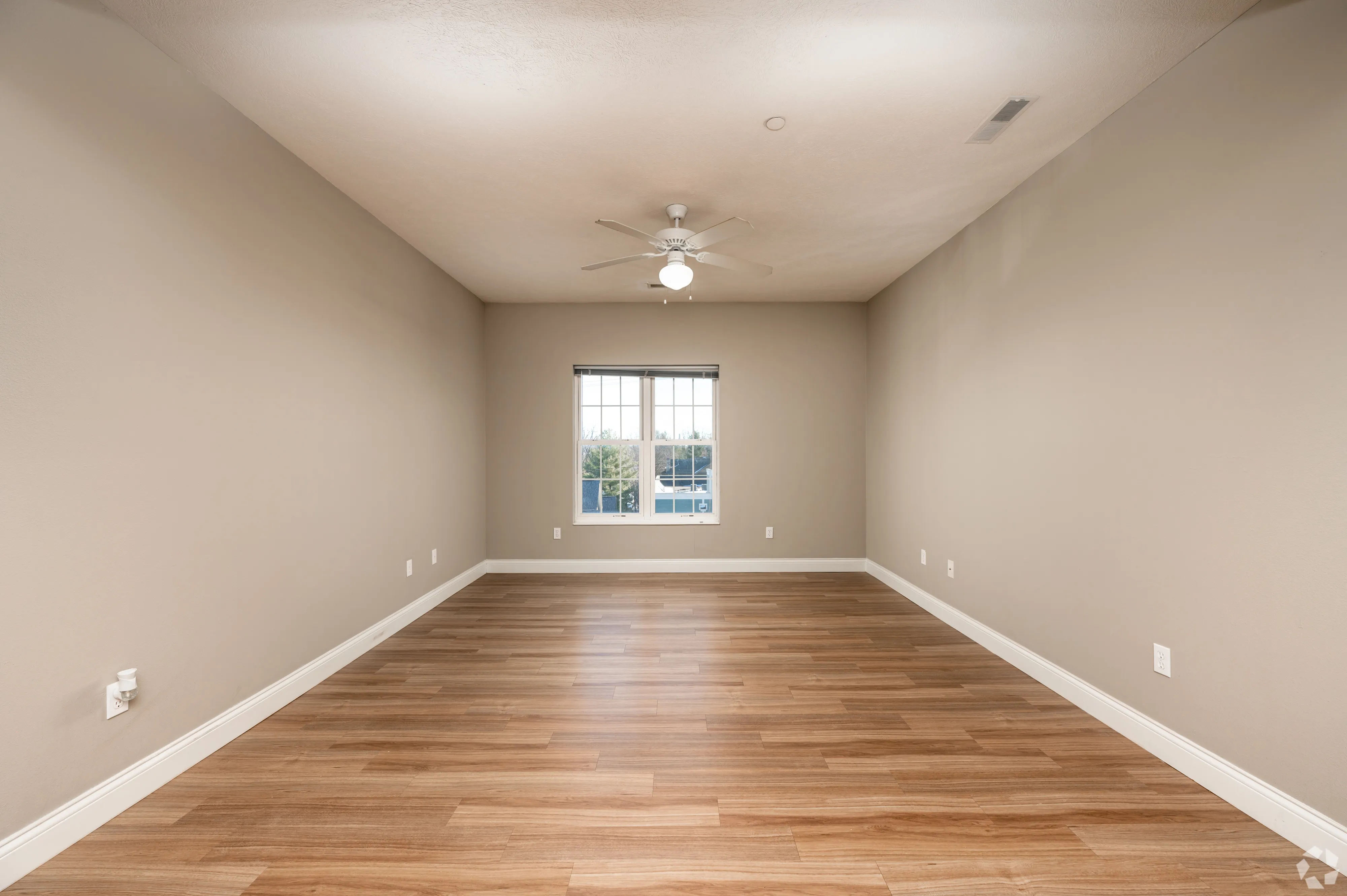 Spacious living area at 7 Ten featuring wide-plank wood-style flooring, neutral walls, and a large window for natural light.
