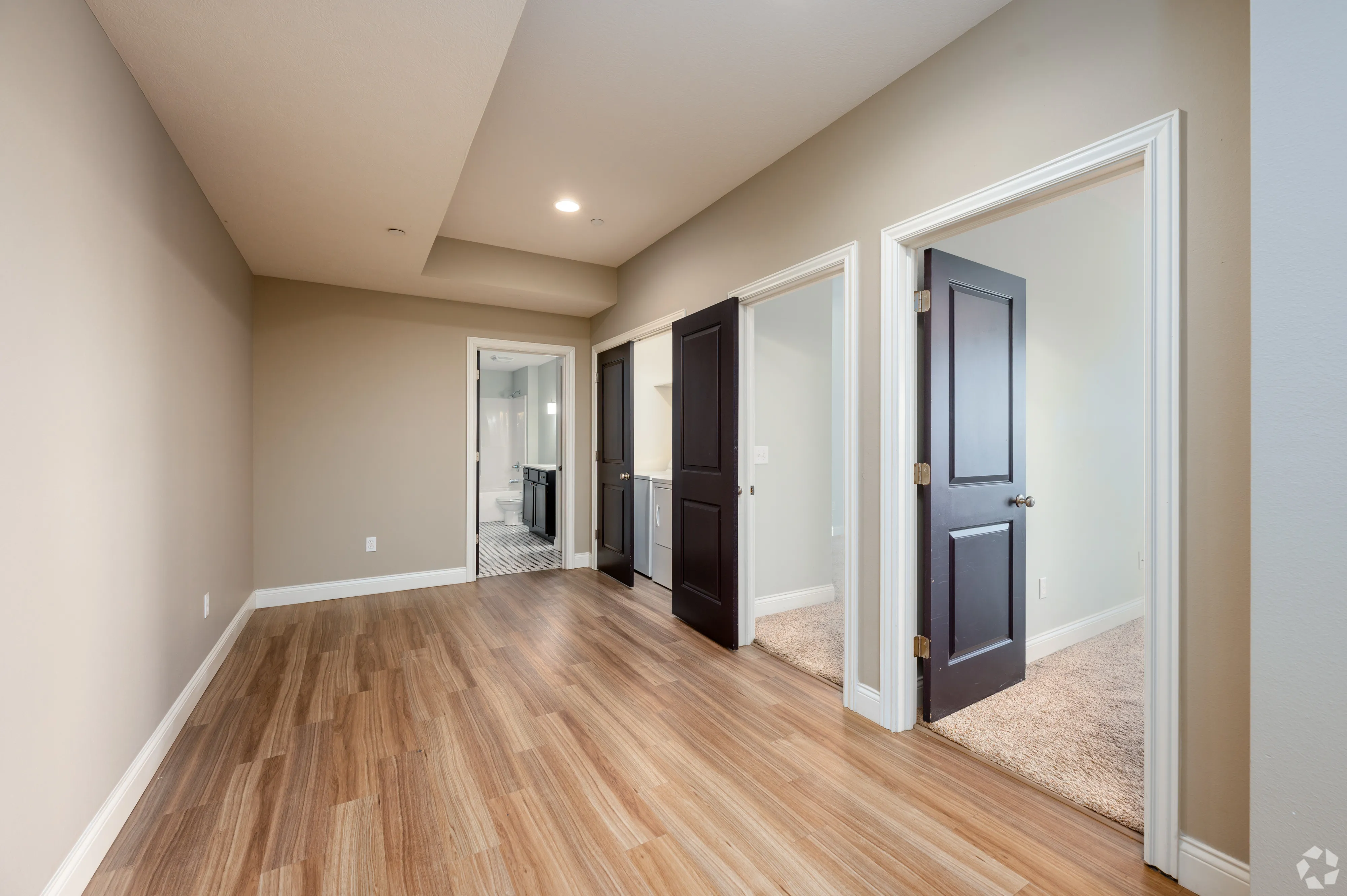 Interior hallway of a 7 Ten apartment with wood-style flooring leading to bedrooms and a bathroom with dark wood doors.