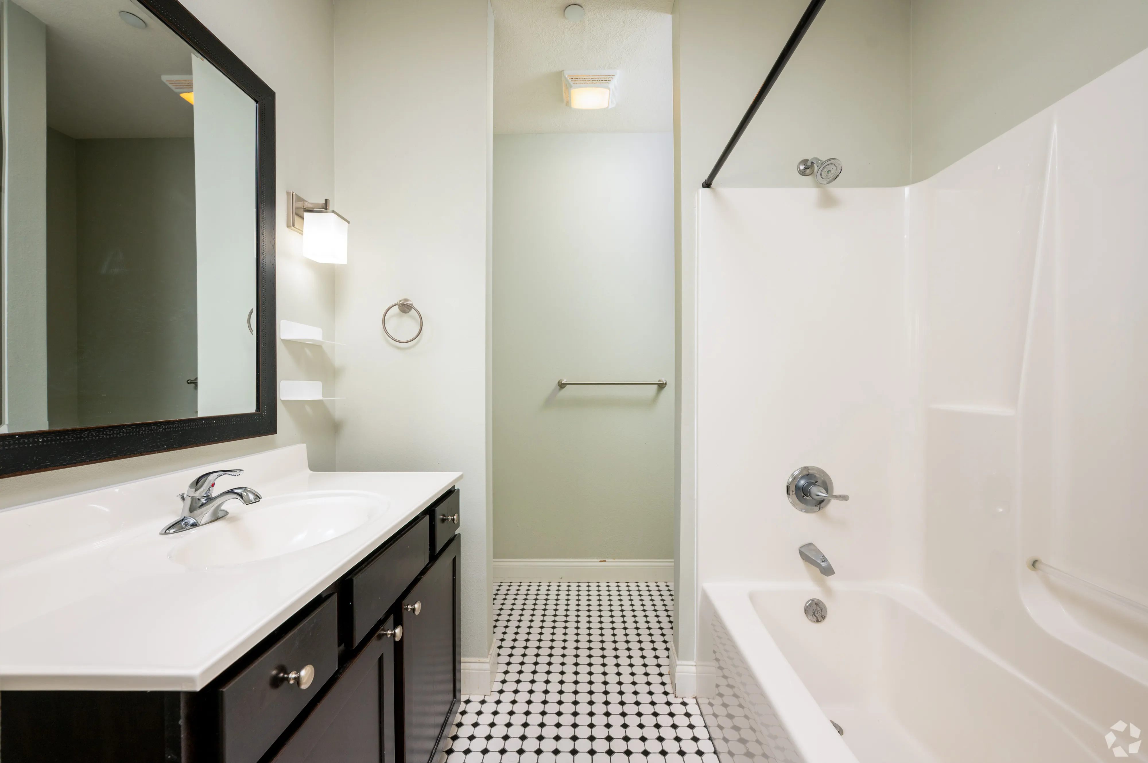 Modern bathroom at 7 Ten with a white bathtub and shower surround, black framed mirror, and decorative tile flooring.