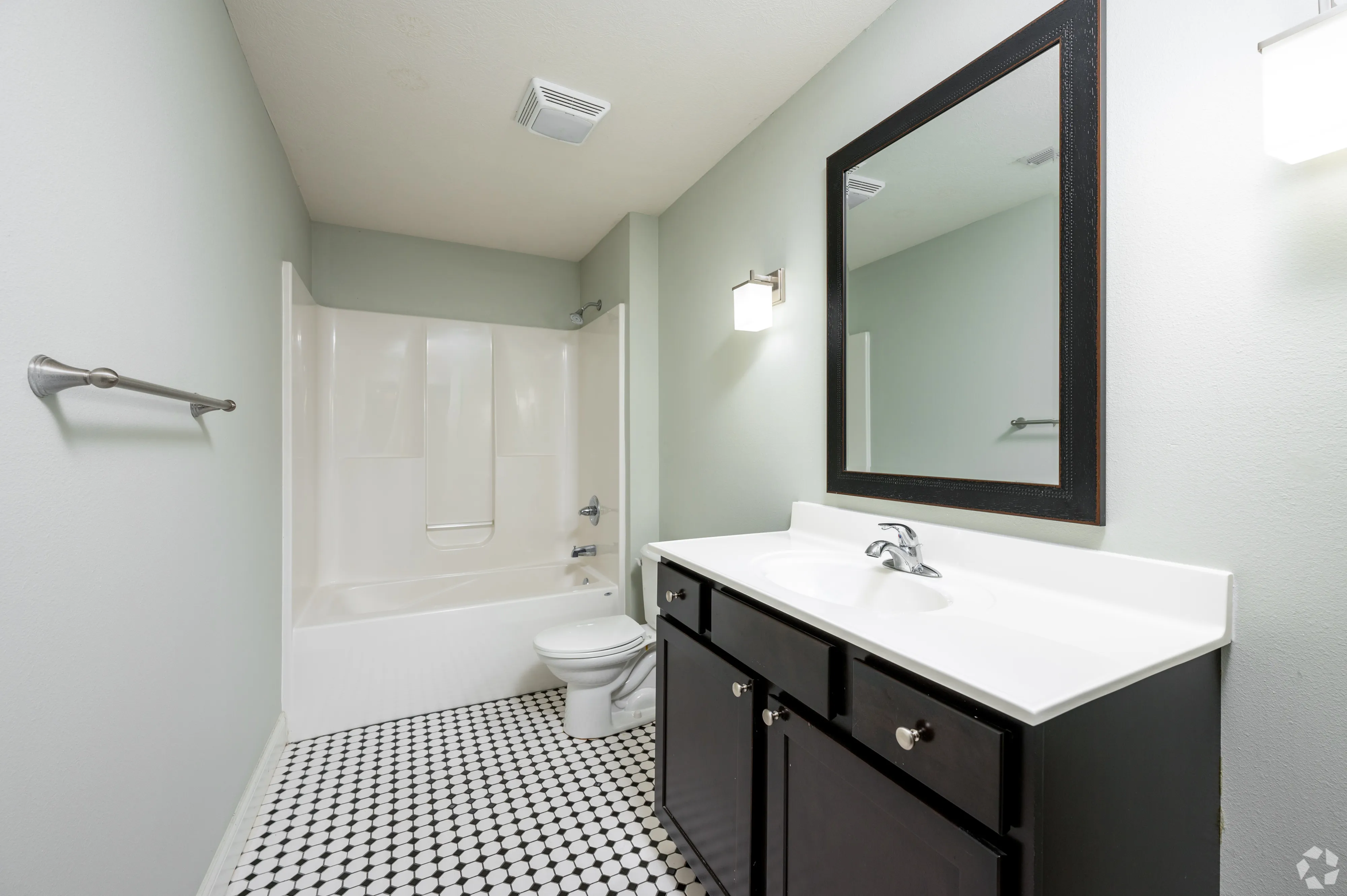 Modern bathroom vanity at 7 Ten with dark cabinetry, white countertop, large framed mirror, and decorative tile flooring.