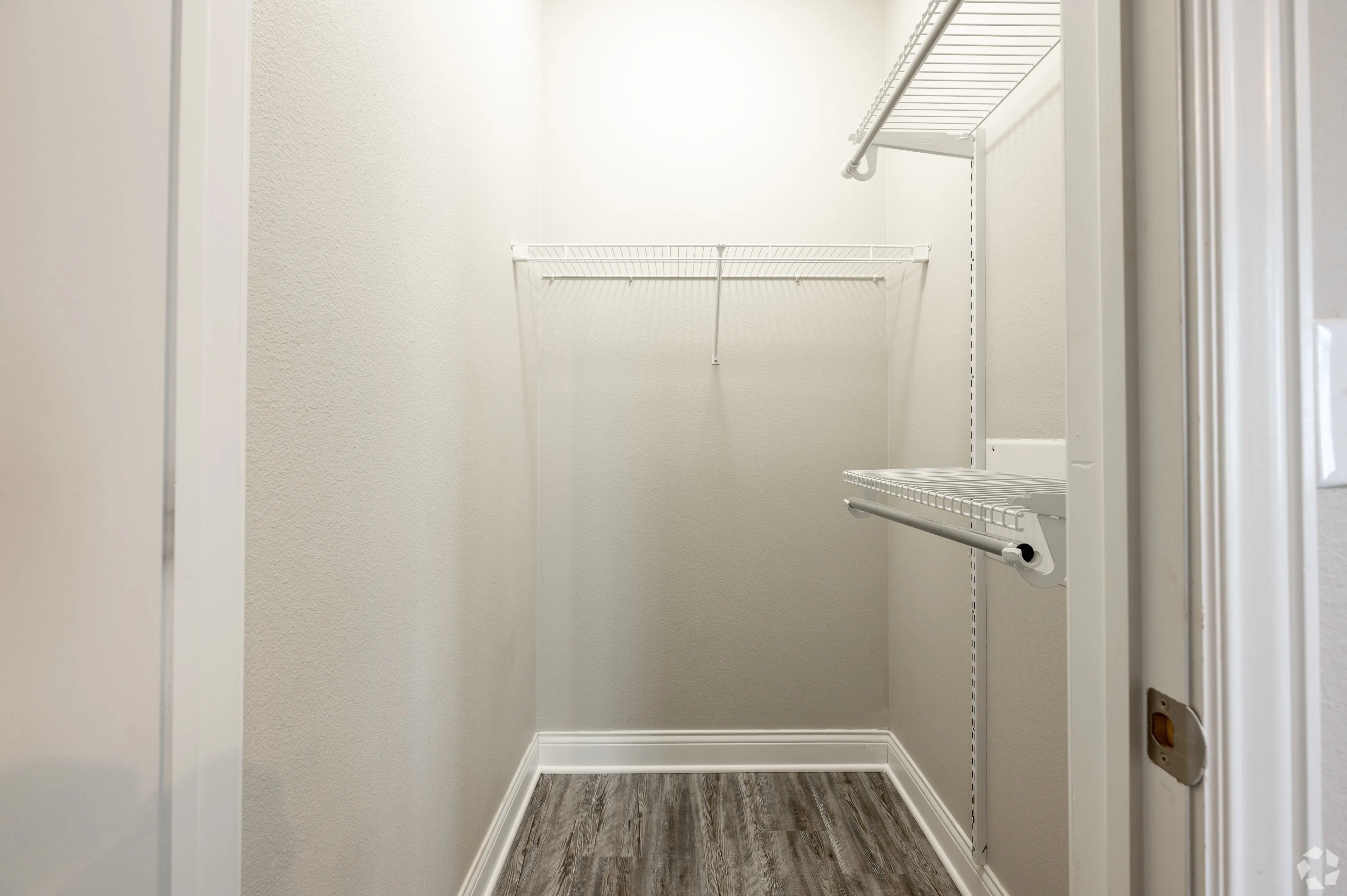 Walk-in closet at 9 North featuring built-in white wire shelving and hanging rods with wood-style flooring.