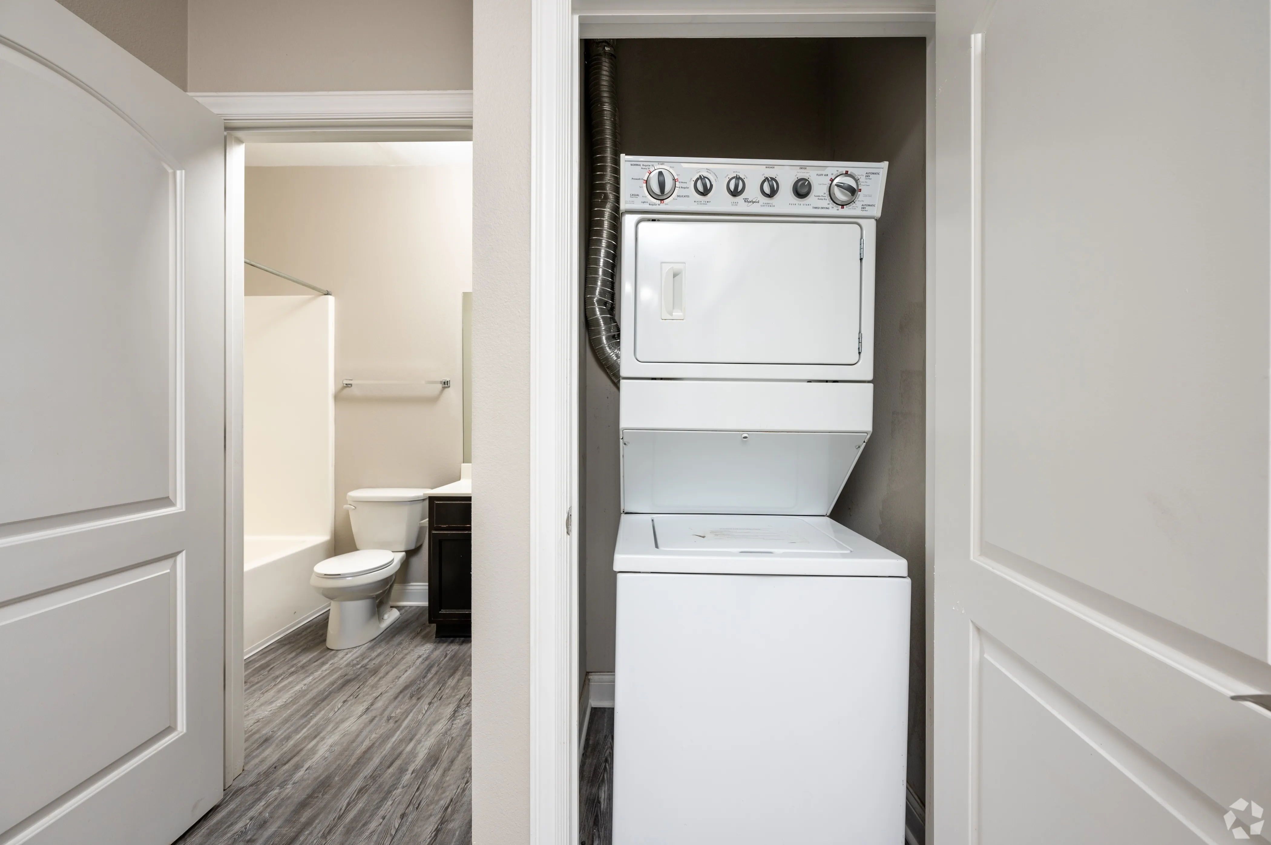 In-unit laundry closet at 9 North featuring a white stacked washer and dryer unit and grey wood-style plank flooring.