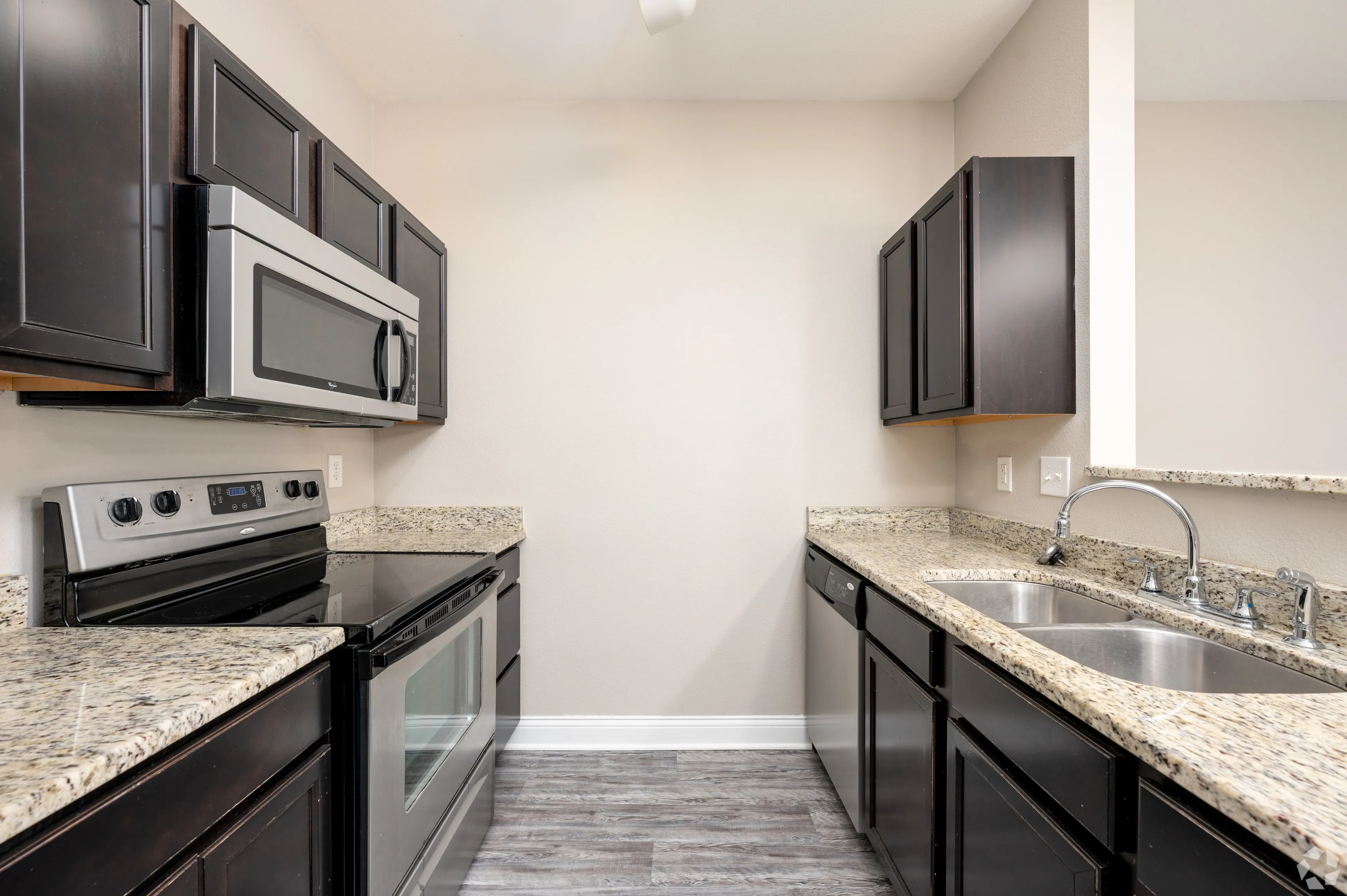 Modern galley kitchen at 9 North featuring dark wood cabinetry, granite countertops, and stainless steel appliances.