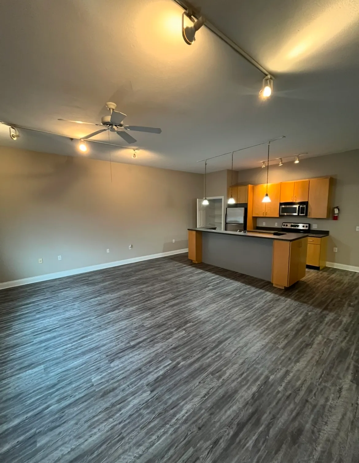 Spacious apartment living room at Lofts on College with recessed track lighting, a ceiling fan, and grey wood-plank flooring.