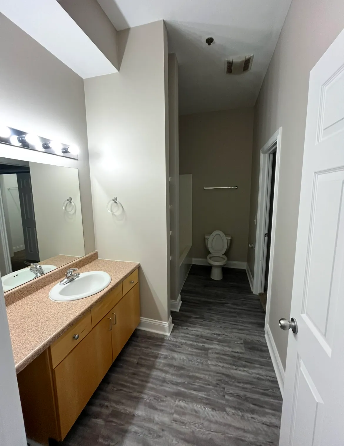 Large bathroom at Lofts on College with a wide light-wood vanity, neutral countertops, and modern grey wood-style flooring.