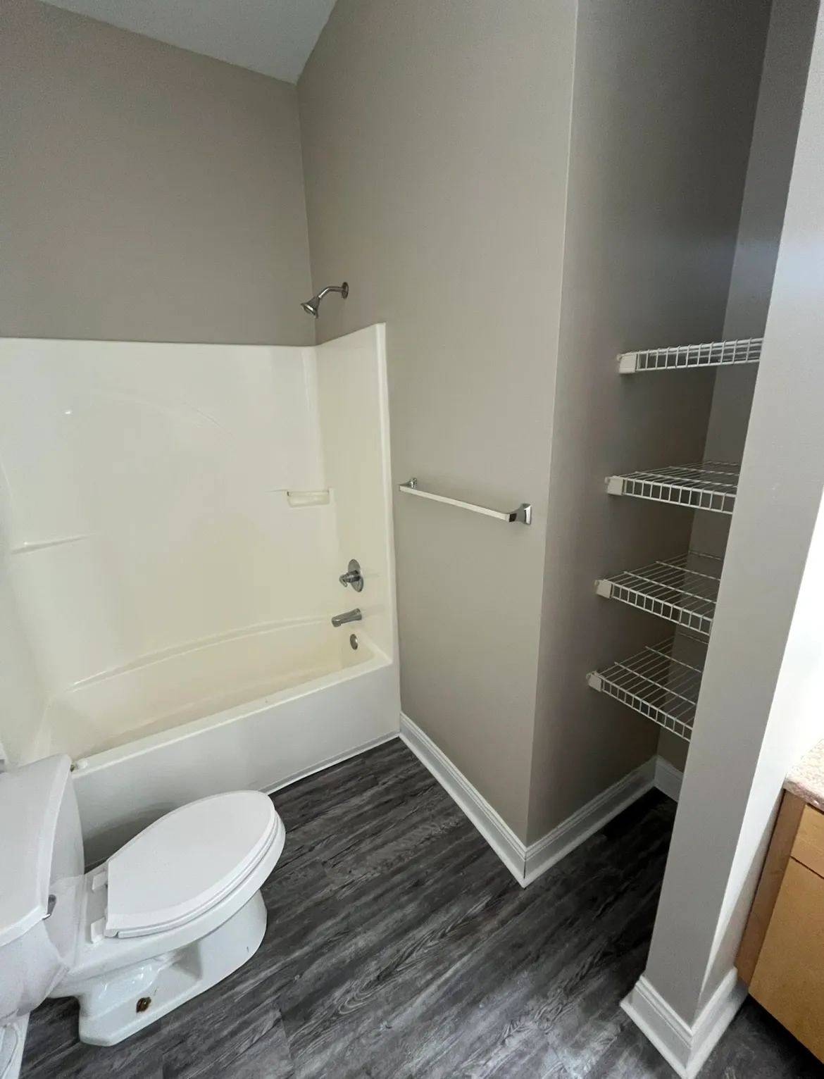 Apartment bathroom showing a white bathtub-shower combination, modern grey flooring, and built-in wire shelving for storage.