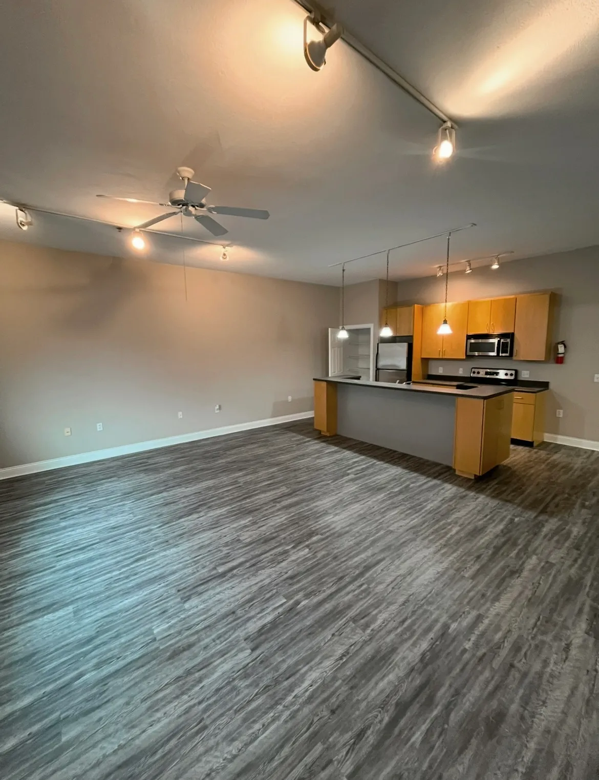 Spacious apartment living room at Lofts on College with recessed track lighting, a ceiling fan, and grey wood-plank flooring.