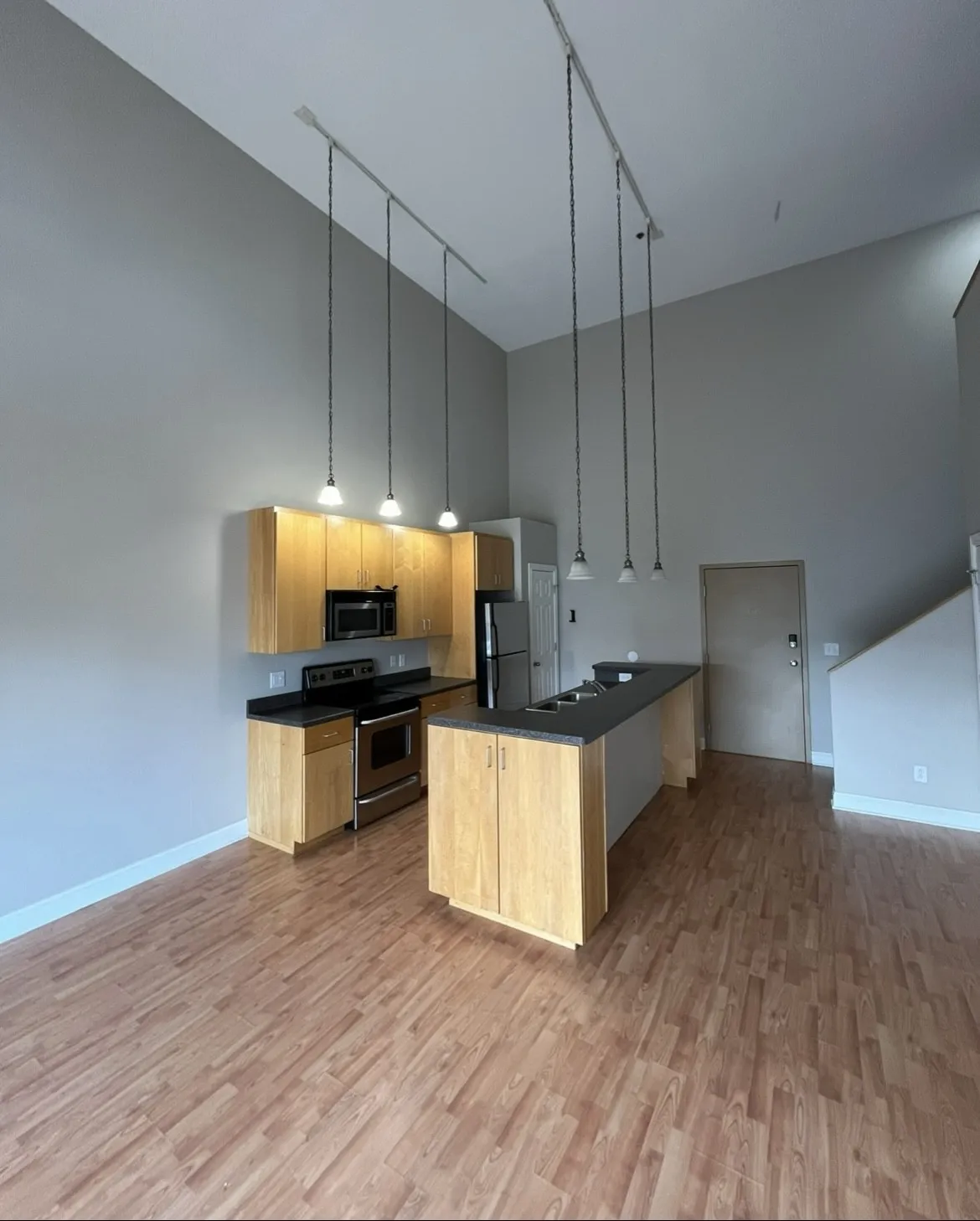 Modern loft kitchen with high ceilings, light wood cabinetry, track lighting, and black countertops at Lofts on College.