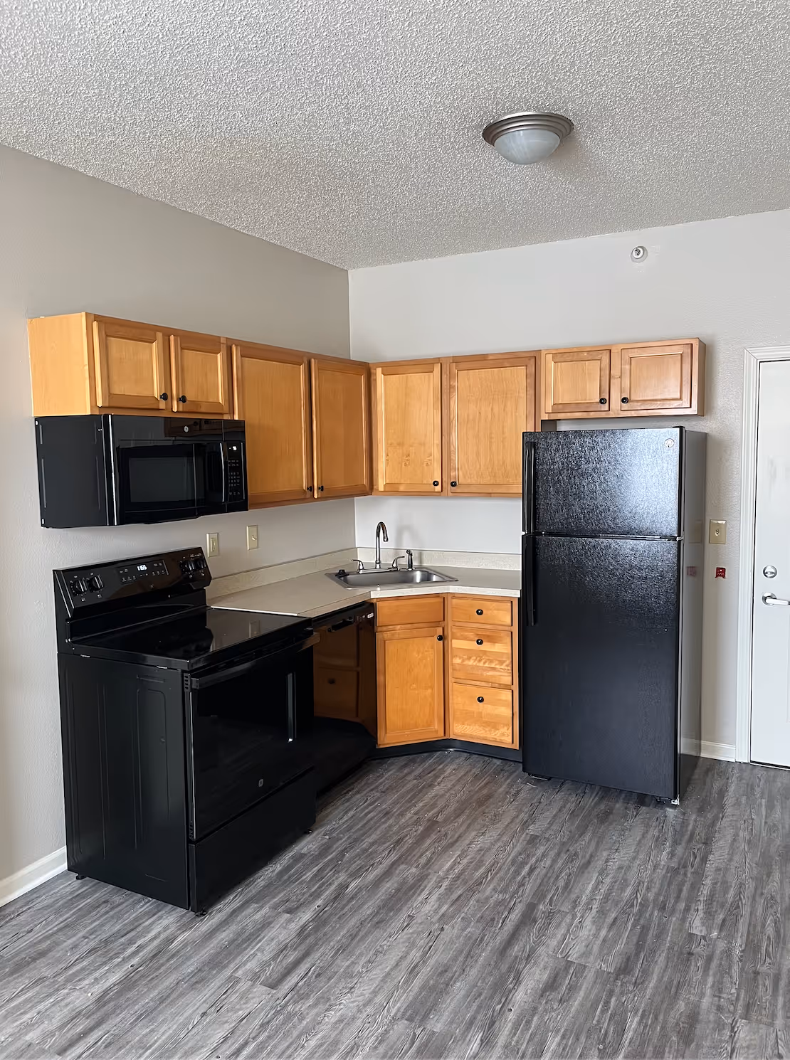 Detailed view of a kitchen at The Northern with a black refrigerator, microwave, and electric stove paired with warm wood cabinets.