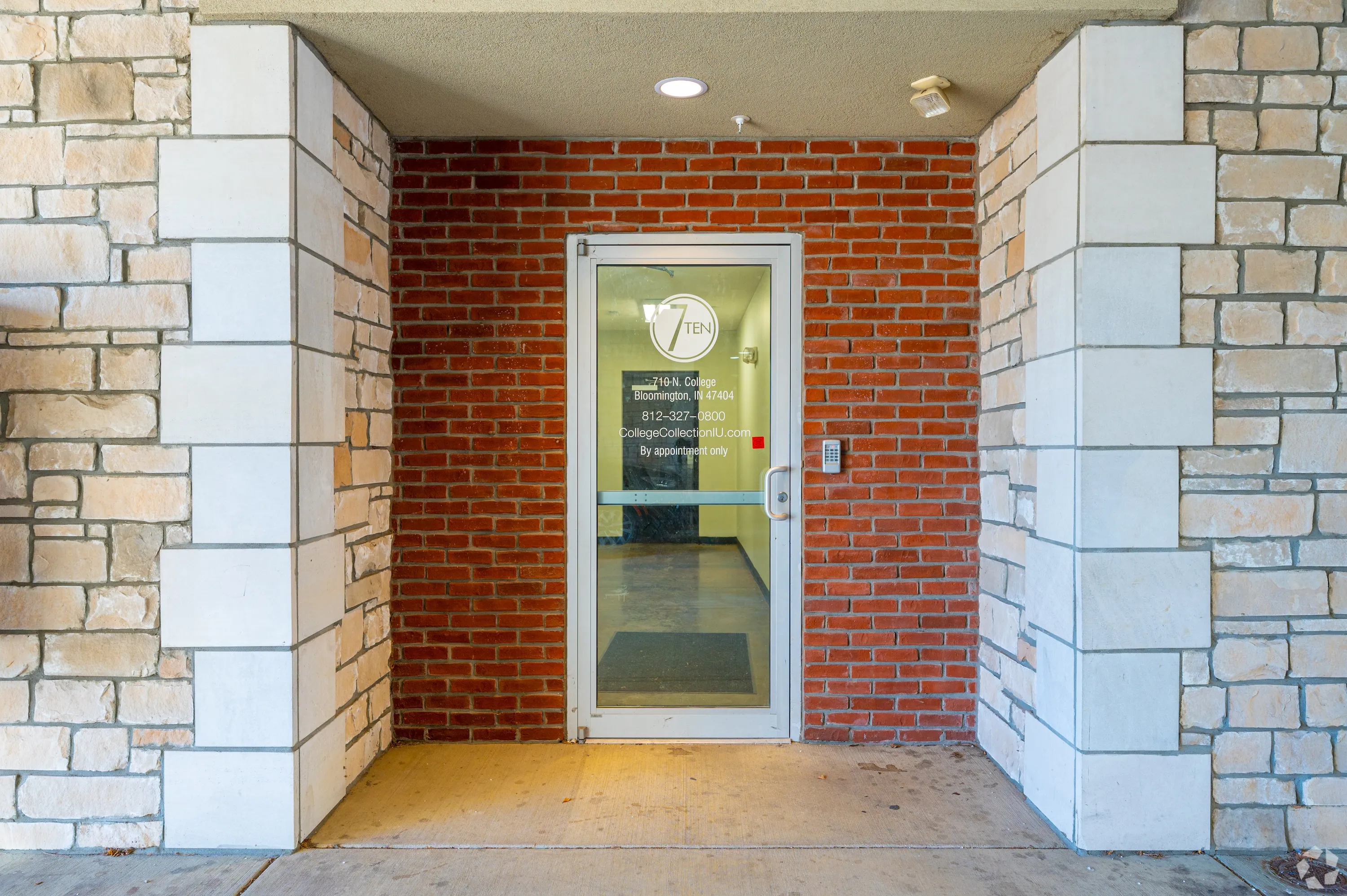 Direct exterior view of 7 Ten apartment building at 710 N College Avenue, featuring red brick and stone with covered parking entrance.
