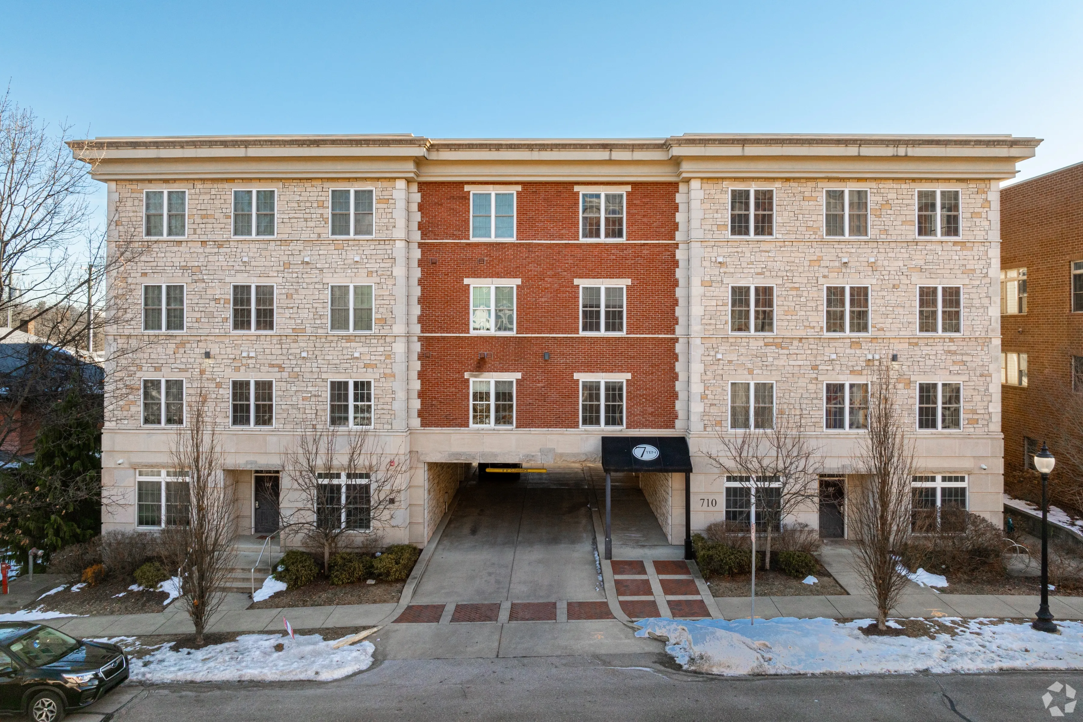 Direct exterior view of 7 Ten apartment building at 710 N College Avenue, featuring red brick and stone with covered parking entrance.