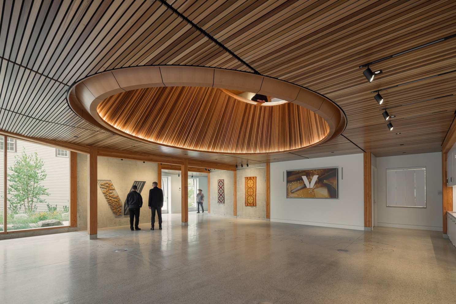 A mass timber wooden ceiling with a well-designed circular vent where people can look down into this floor. Mass timber posts and beams frame the room.