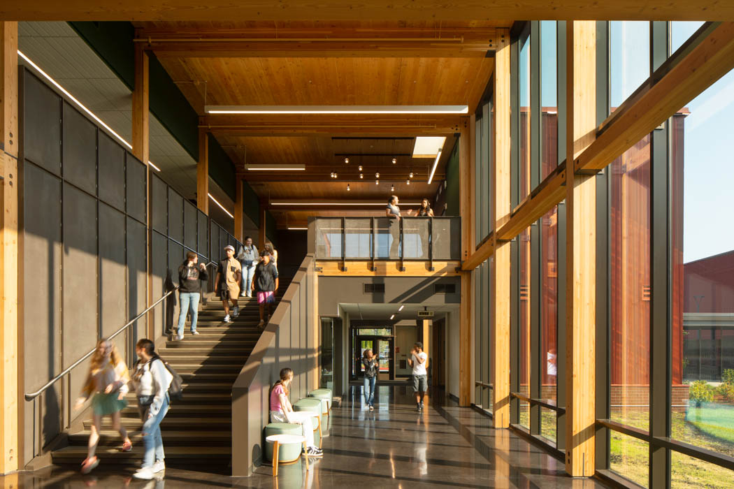Students in an open space hallway talking in ASL. Exposed mass timber and windows make light everywhere in the room appear bright. Stairs are wide enough for students to do sign language and walk at the same time. 