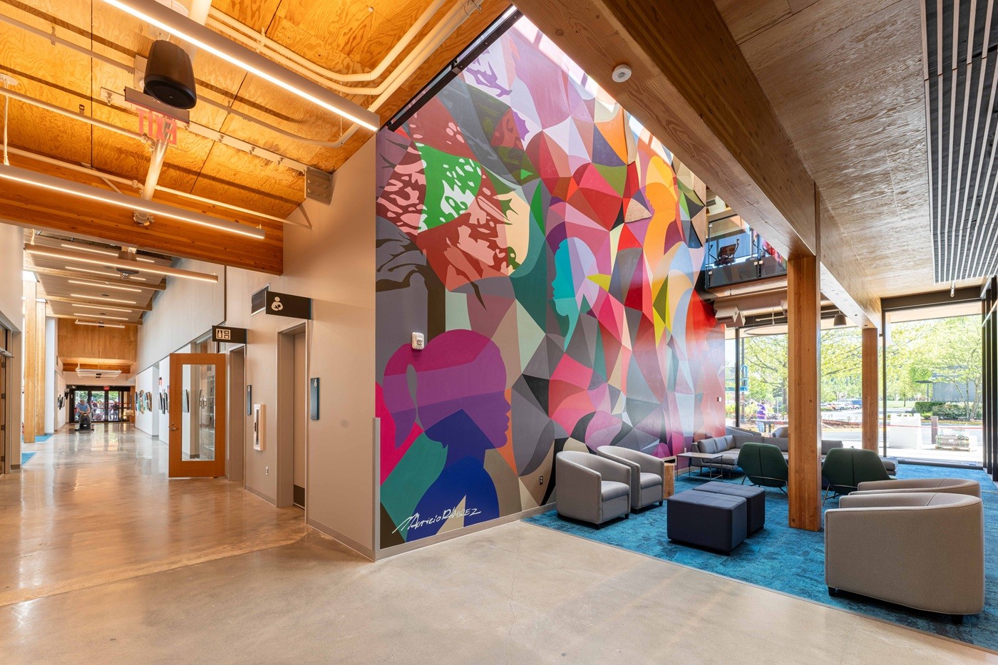 Colorful mural painted with a tree and woman on the wall entry way with mass timber beams and ceiling panels. A baby and mother room and a restroom are down the hallway.