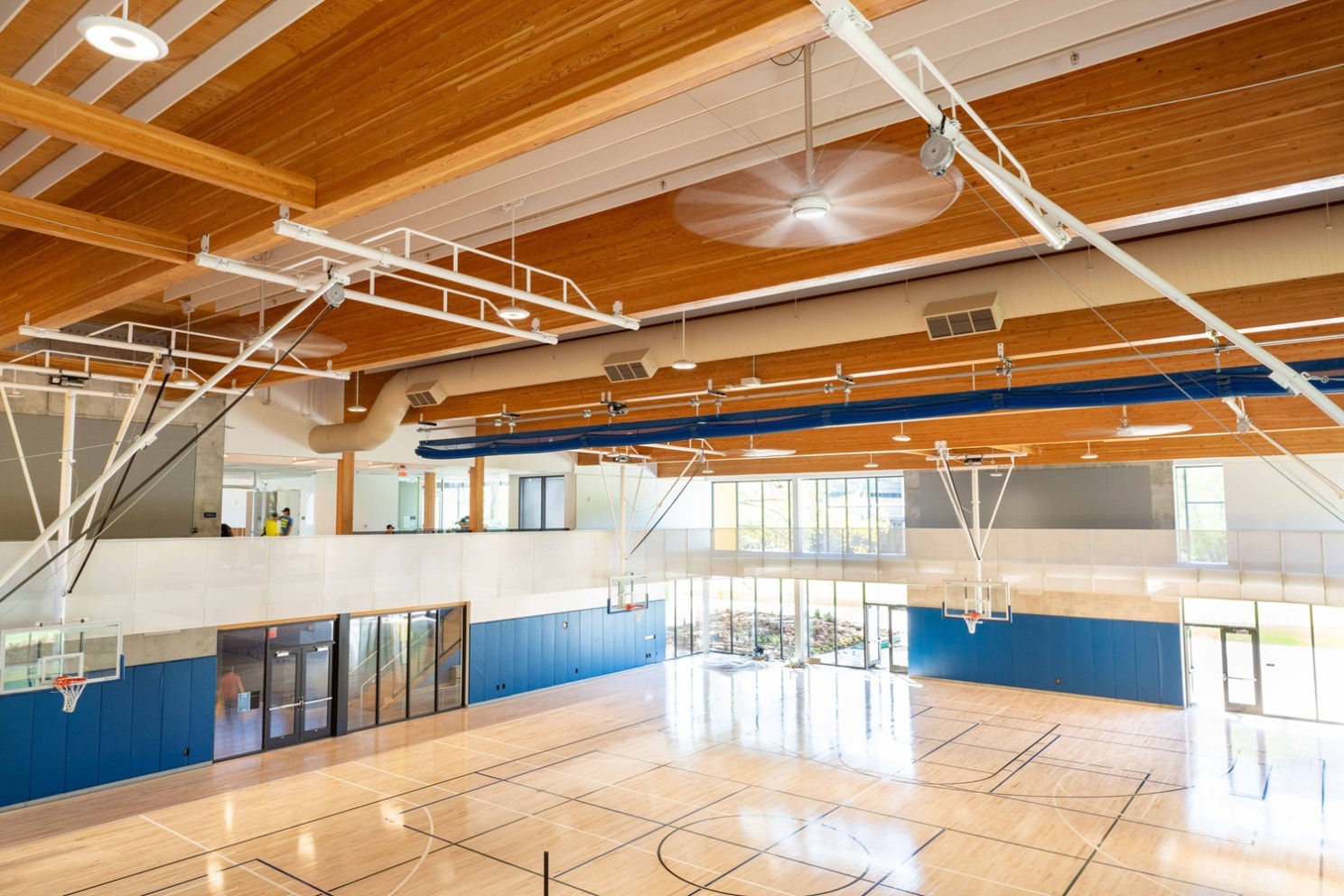 An amazing mass timber ballcourt gym with beams and ceiling panels. White duct work and the blue mats on the walls give this gym some color.