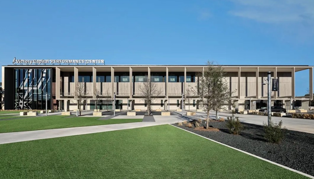 The exterior of the Victory Capital Performance Center with green grass and trees without leaves on them. 