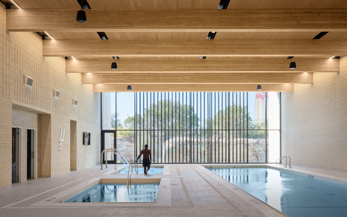 A swimming pool and hot tub room with exposed mass timber ceilings looking out floor to ceiling windows. 