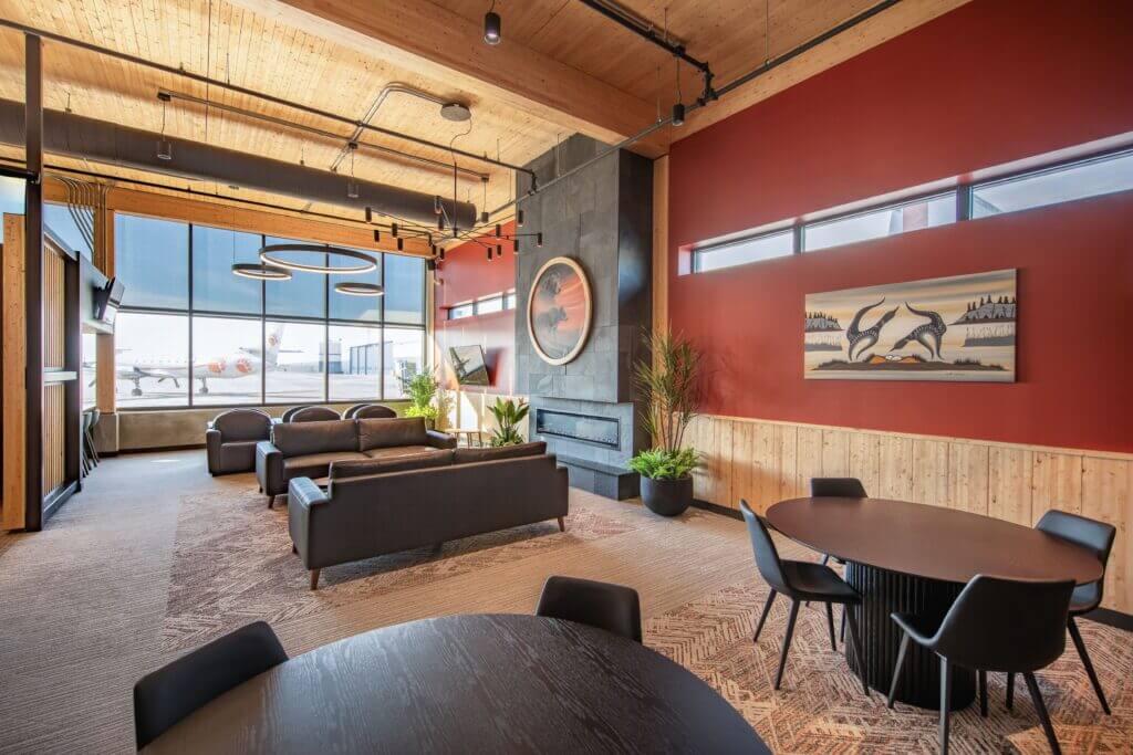 An airplane seen through a window and exposed mass timber ceilings in a lobby with tables and chairs to sit at. 