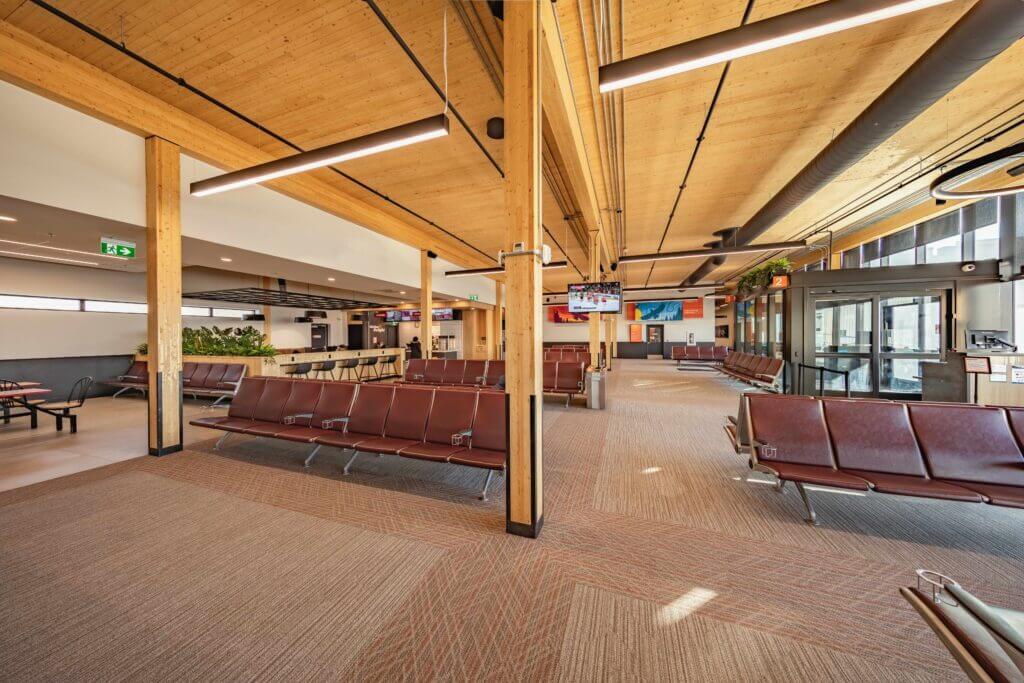 A long airport gate with chairs in rows and exposed mass timber ceilings and beams. 