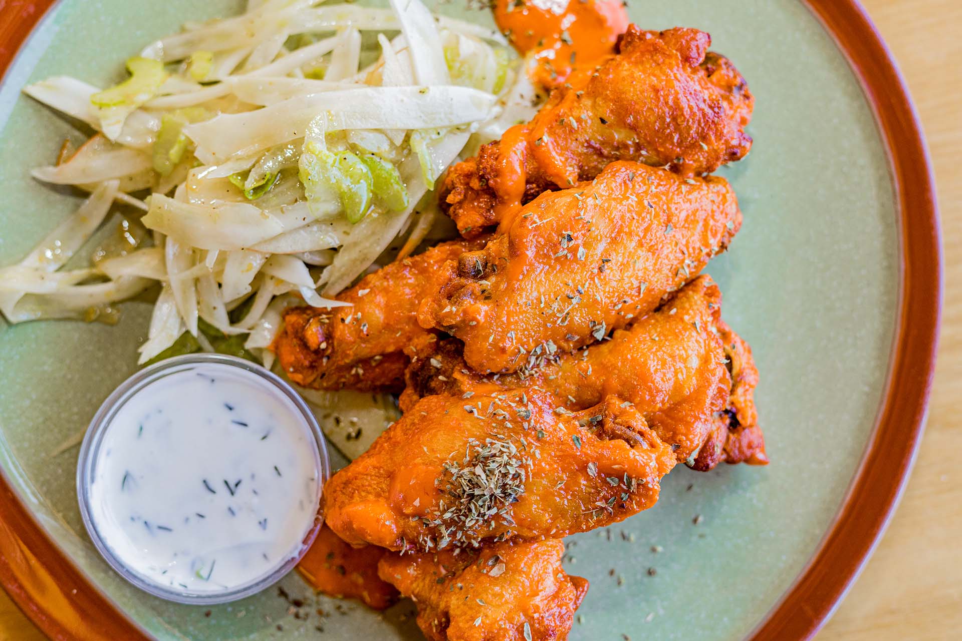 A plate of wings with a side of dressing and salad.