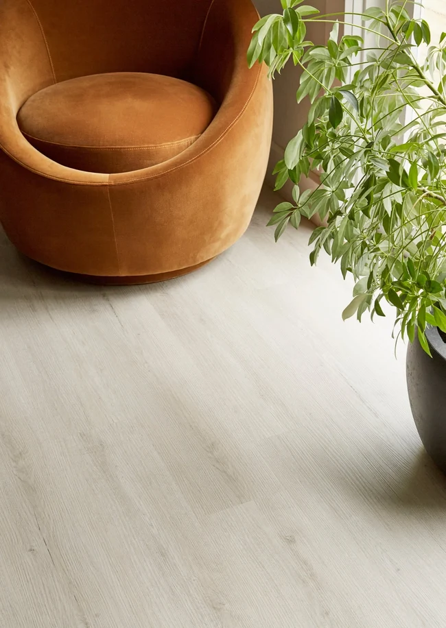 Whitewashed oak hybrid SPC flooring beside a tan armchair