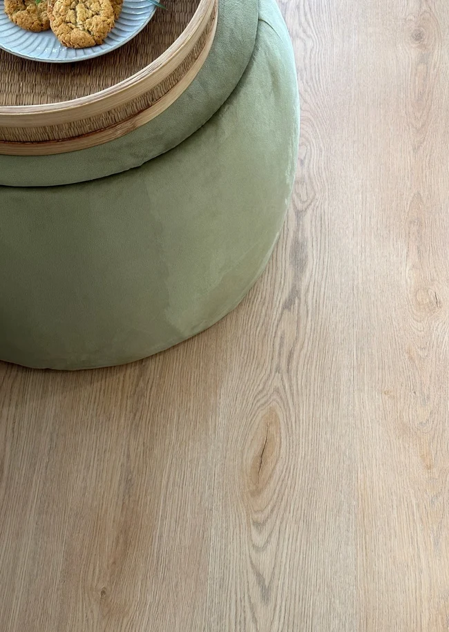 Light oak hybrid SPC flooring in a living room with a green ottoman