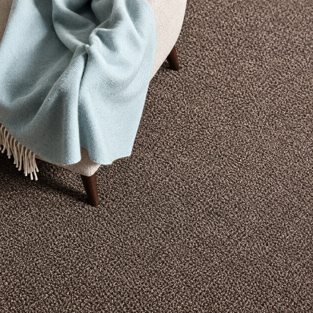 Close view of a mocha brown loop pile carpet with a pale blue throw