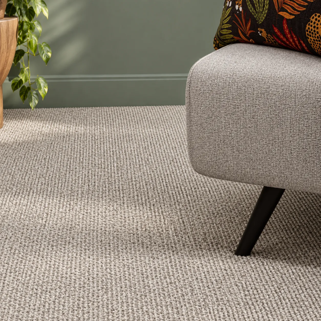 Close view of a pale grey loop pile carpet beside an upholstered chair