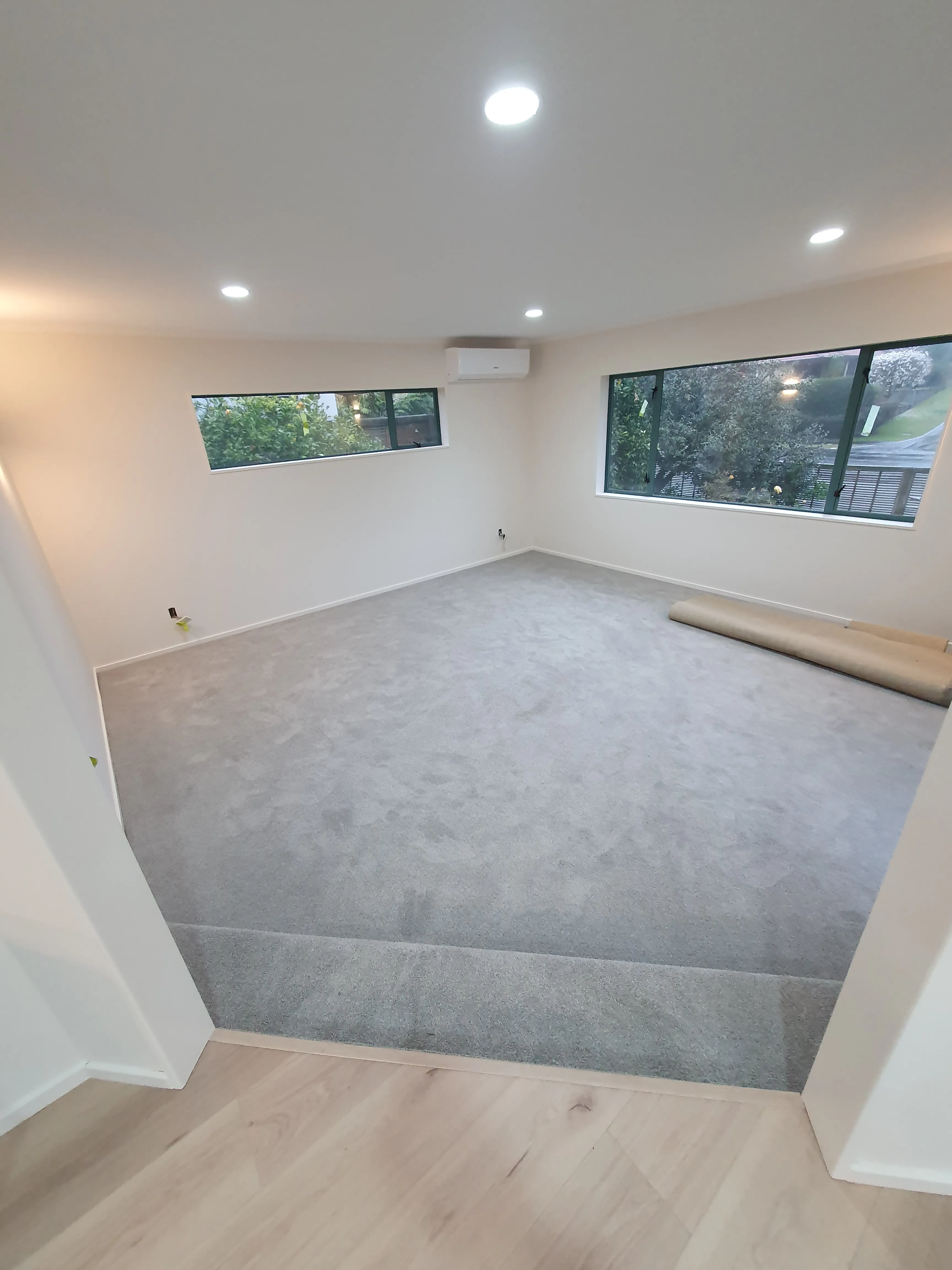Grey cut pile carpet laid in a new build living room, meeting timber flooring at the doorway