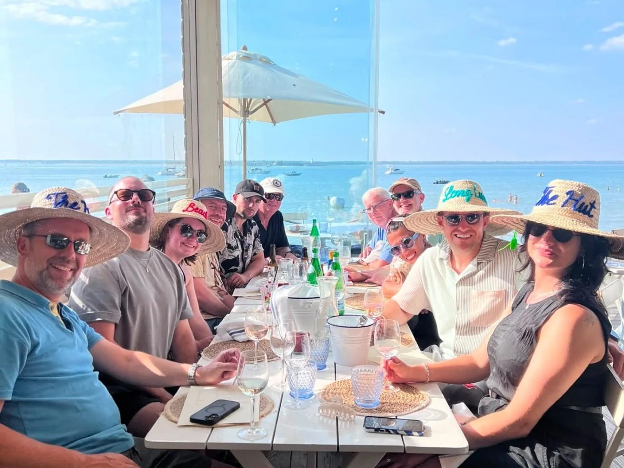 The INCEPTION team at a long beachside lunch table in straw hats