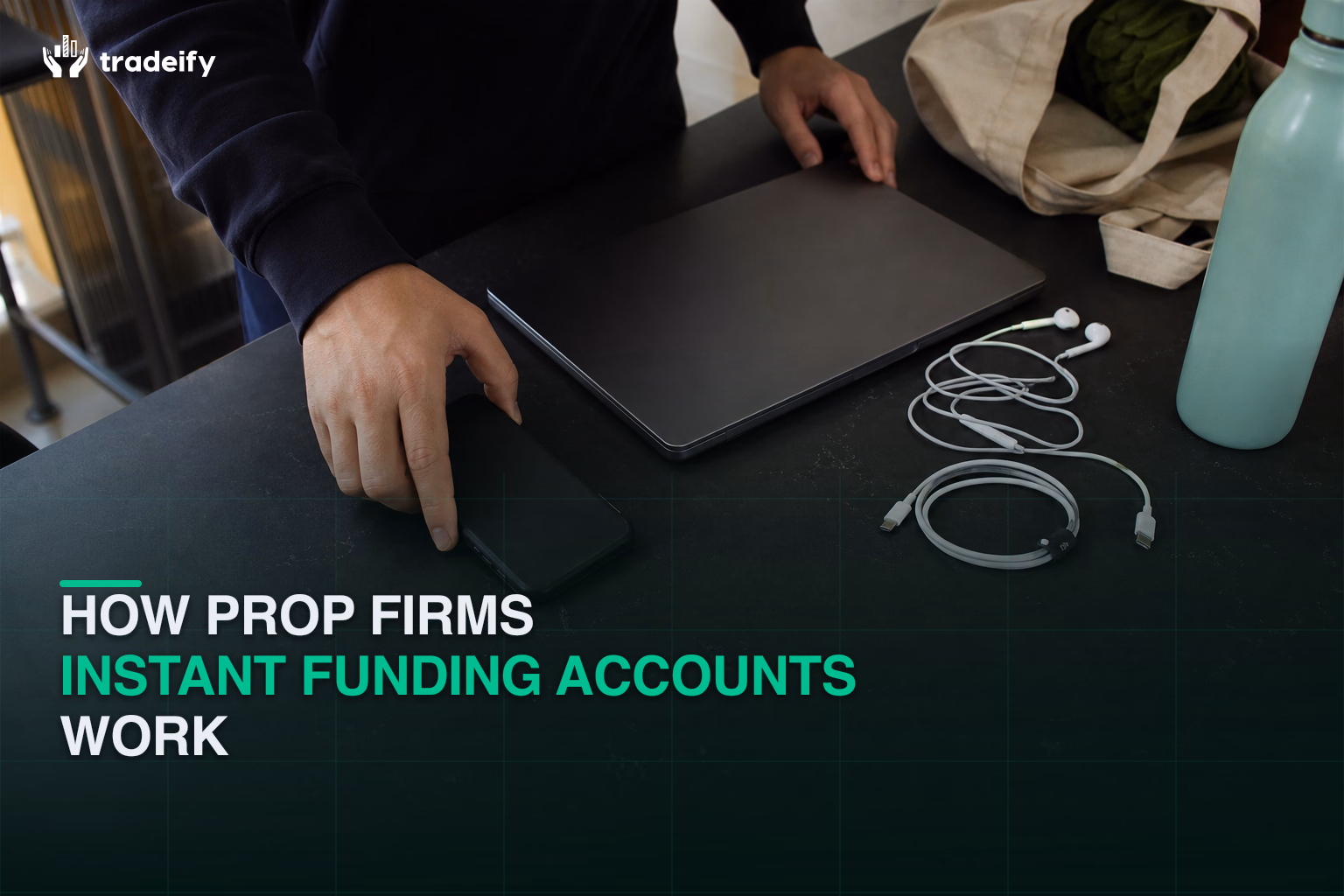 Trader organizing a phone, closed laptop, earbuds, and charging cable to begin an instant funded account workflow