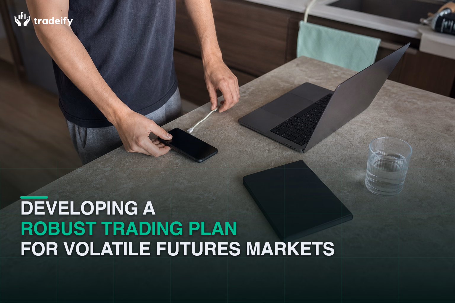 Trader arranging a phone, charging cable, and closed notebook before a focused futures session at a kitchen counter