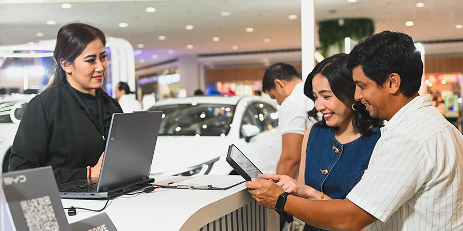 Couple reviewing car loan options with sales representative at dealership, highlighting financing choices for electric and traditional vehicles in the Philippines