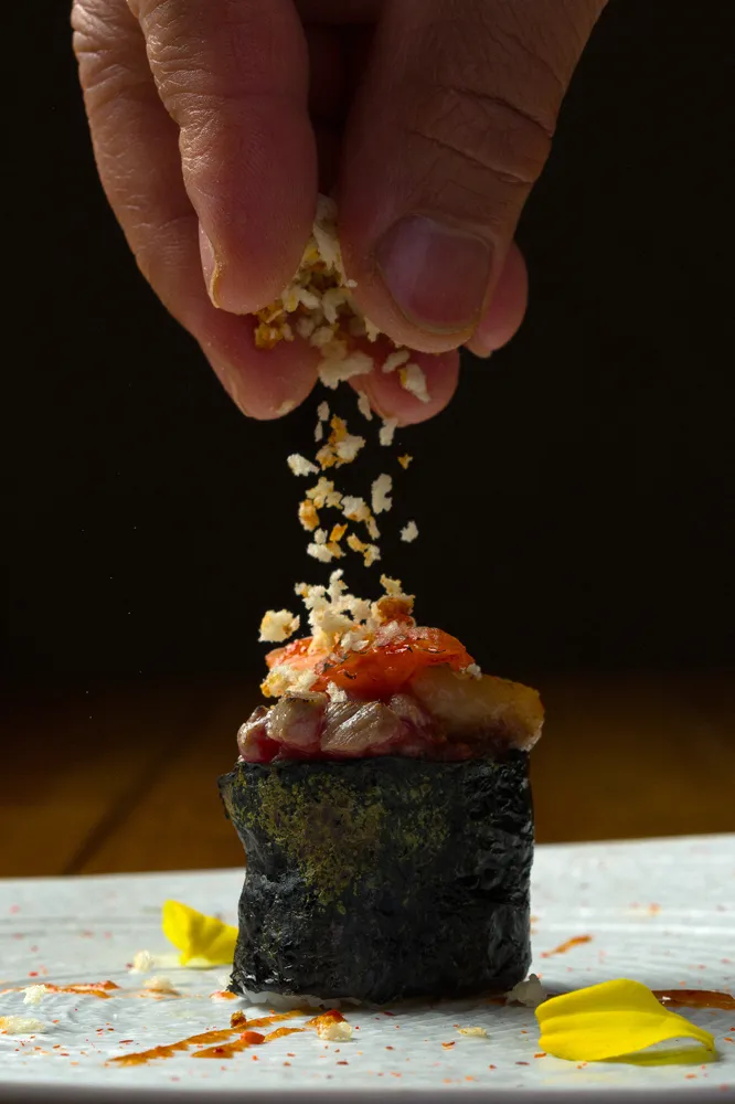 Nigiri sushi con pescado amarillo cubierto con tiras rojas delgadas sobre plato negro.