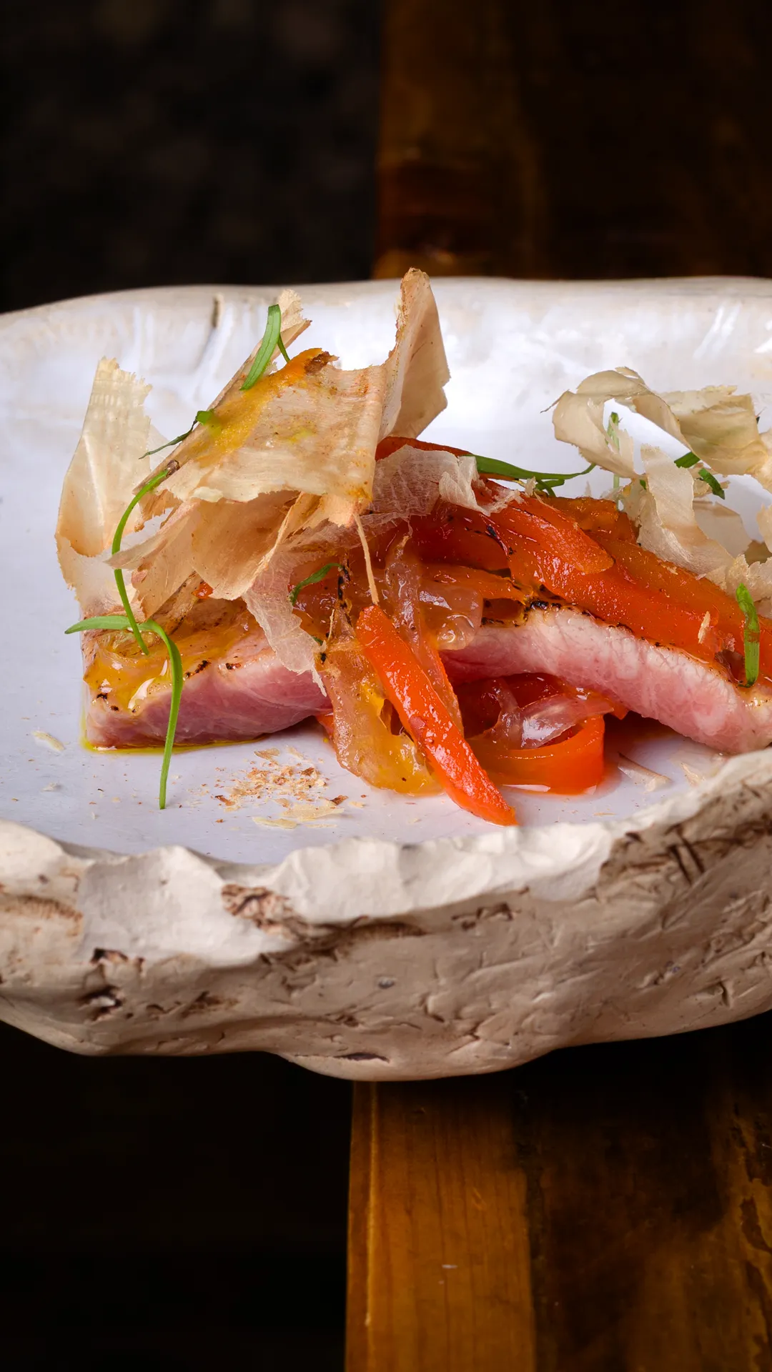 Plato artesanal con rebanada de carne rosada, pimientos rojos y finas láminas de adorno verde y translúcido.