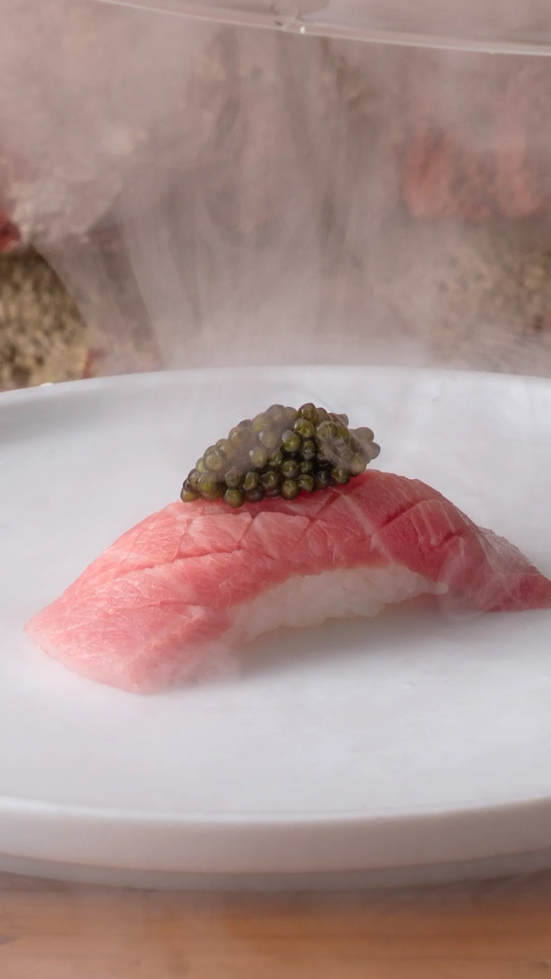 Tres pequeñas porciones de sushi gourmet presentadas en platos cerámicos sobre una hoja verde en una bandeja blanca alargada.