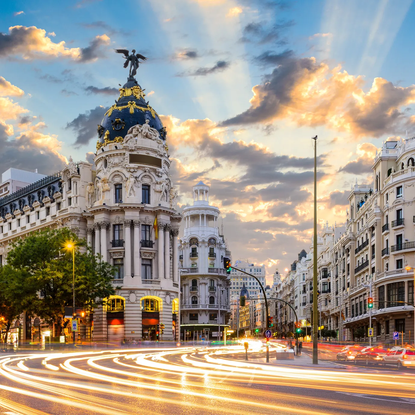 Edificio Metropolis en Madrid con luces de tráfico y estelas de luz al atardecer.