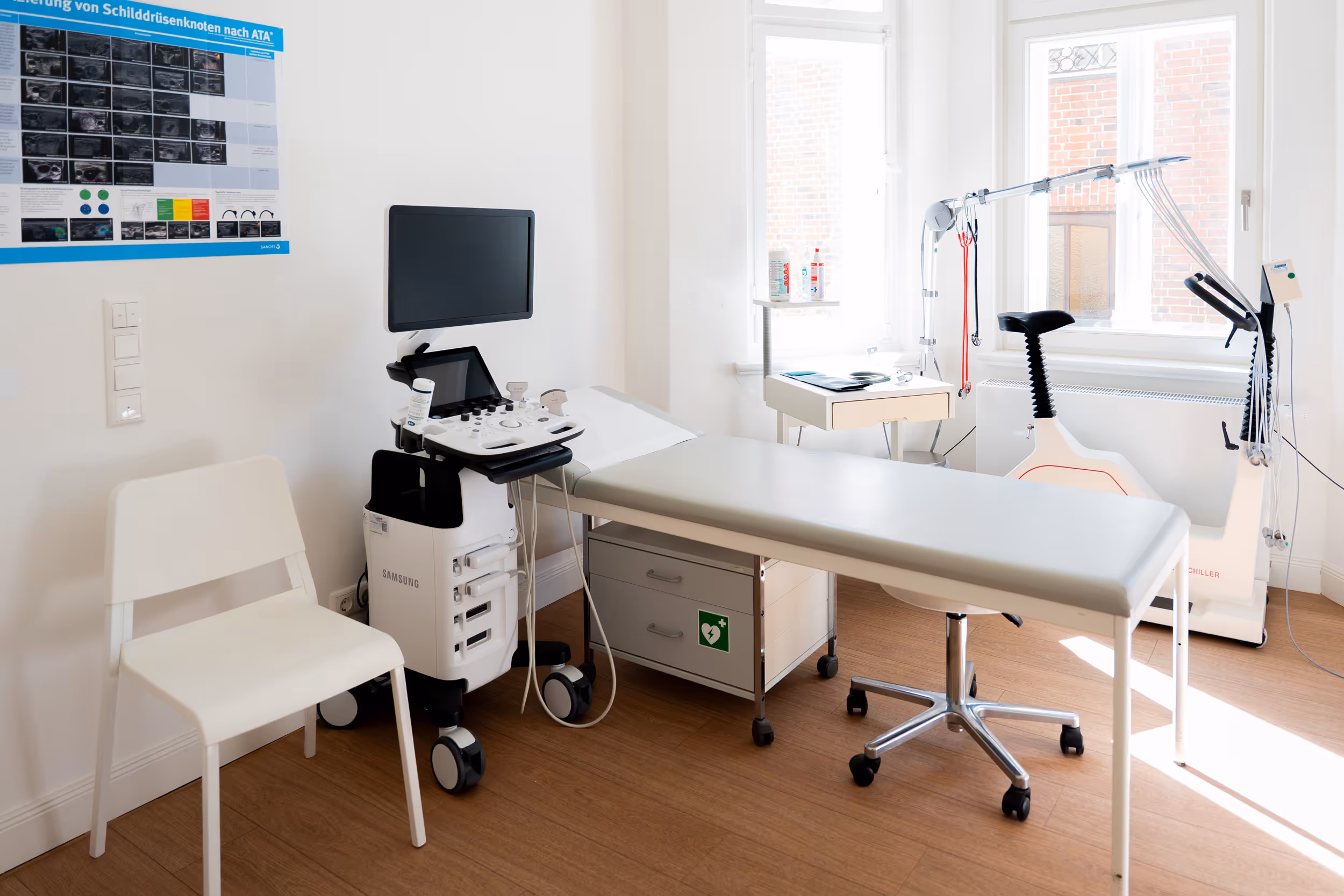 Praxisräume der Hausarztpraxis Dr. Winter in Lüneburg. Heller Behandlungsraum mit Ultraschallgerät, Untersuchungsliege, Stuhl und medizinischem Fahrradergometer.