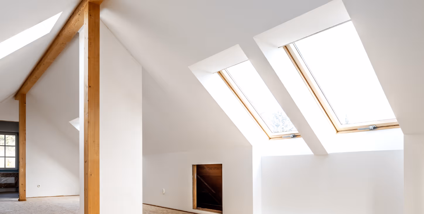 Heller Dachausbau mit zwei großen Dachfenstern und sichtbaren Holzbalken – moderner Innenausbau mit viel Tageslicht.