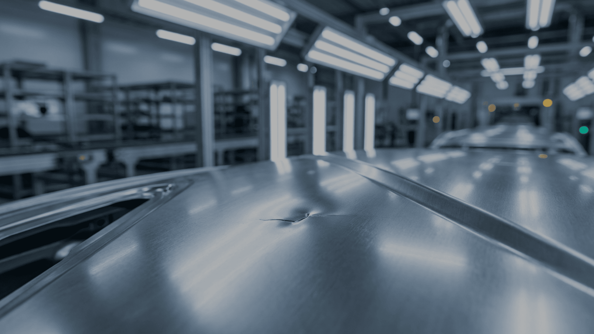 Close-up of a stamped automotive roof panel with a visible dent, photographed under inspection lighting inside a manufacturing line to highlight surface defects.